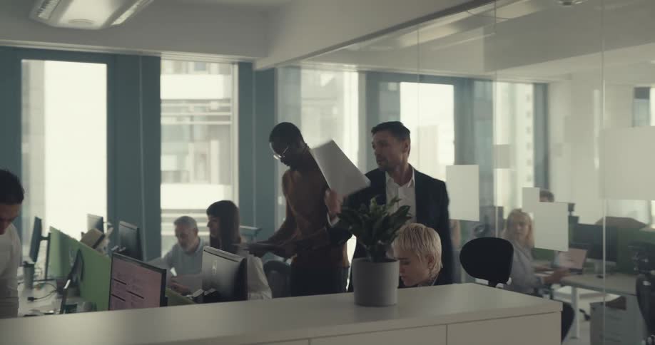 A male throws papers down on a desk in an open cubicle office