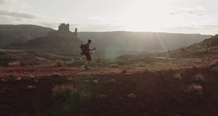 A hiker walks across the desert badlands as the sun shines brightly in the distance