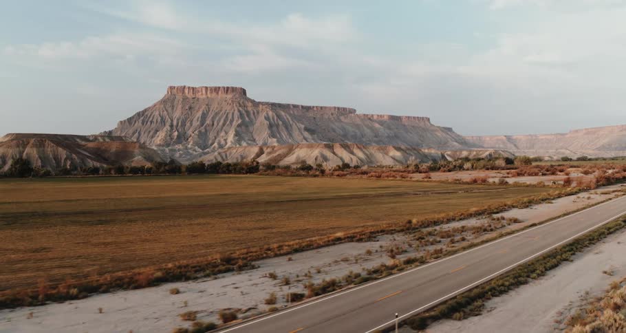 A road traveling through the desert badlands alongside mountains and mesa under a cloudy sky