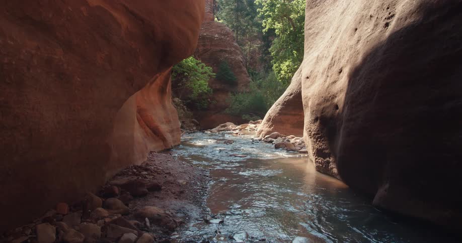 Man hikes along stream through narrow gap between stone walls