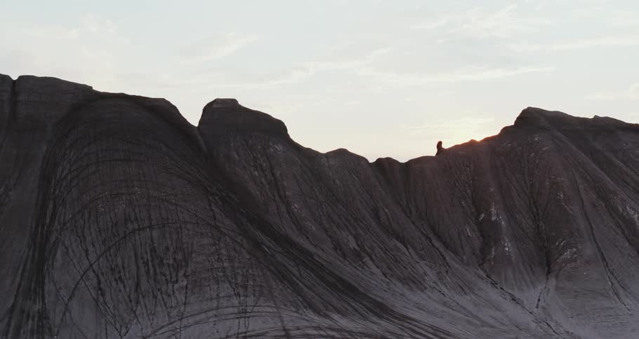 The sun peaks out of a rough mountain ridge under a cloudy sky