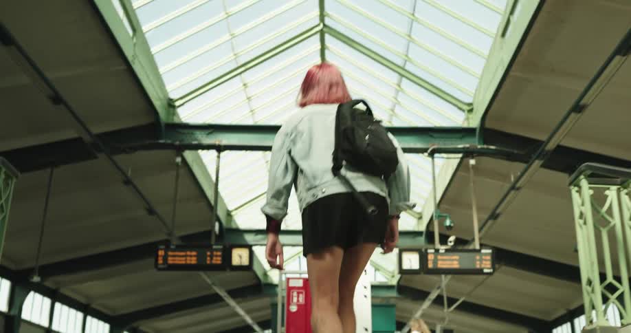 A woman wearing a backpack is walking up the stairs in a train station