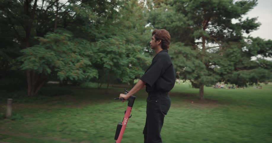 A man is riding on an electric scooter on a sidewalk through a park