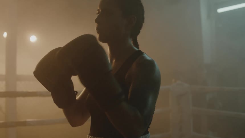 A female boxer claps her boxing gloves together as she stands inside a boxing ring
