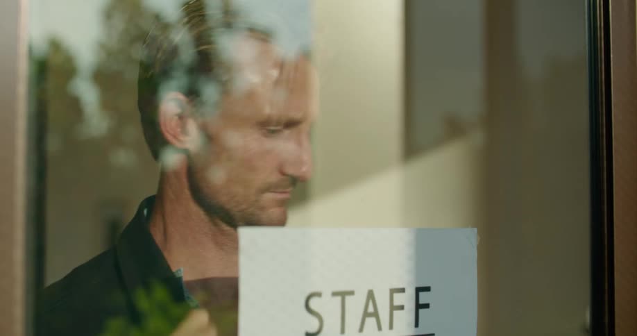 A man hangs a staff needed sign in a window