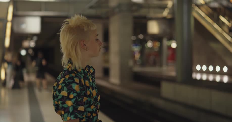 A woman is standing inside a train station and waiting by the track