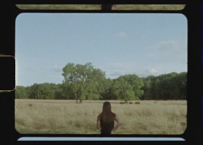 Woman with brown wavy hair and black t shirt walks in the field