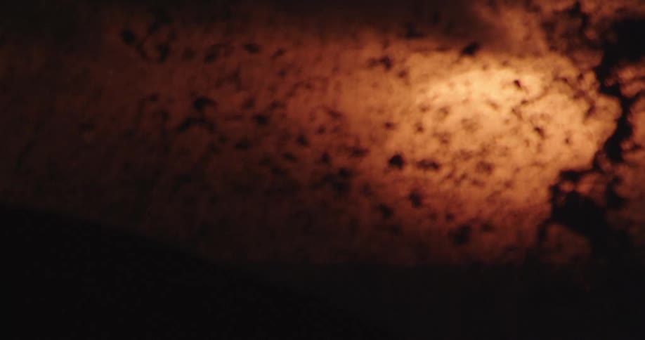 Ocean waves crash splashing in front of the sun setting behind the clouds