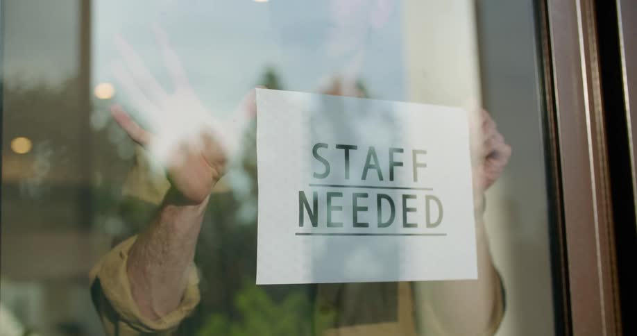 A man sticks a help wanted sign on the inside glass of his business