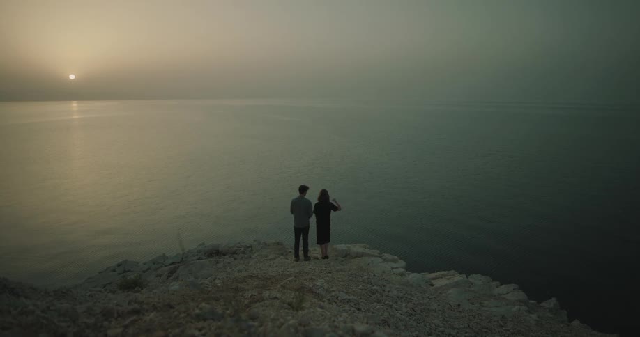 Man and woman are standing by the ocean at dusk