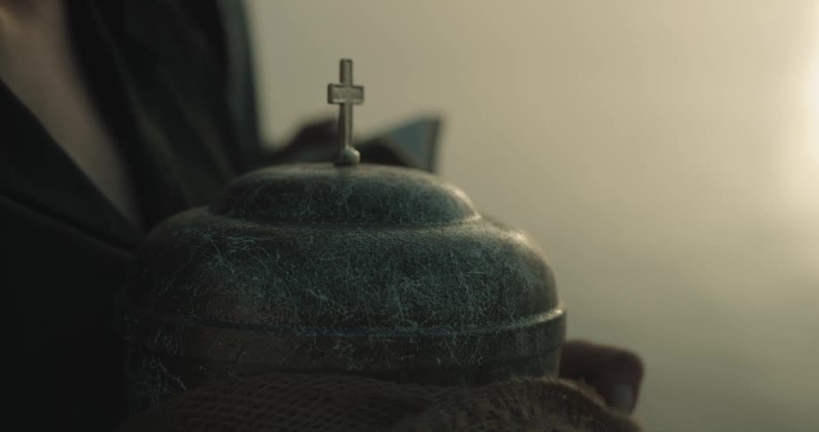 A woman removes burlap surrounding an urn and hands the urn lid to a man next to her