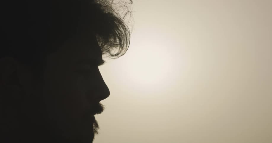 Man with shirt and beard is silhouetted against the sun