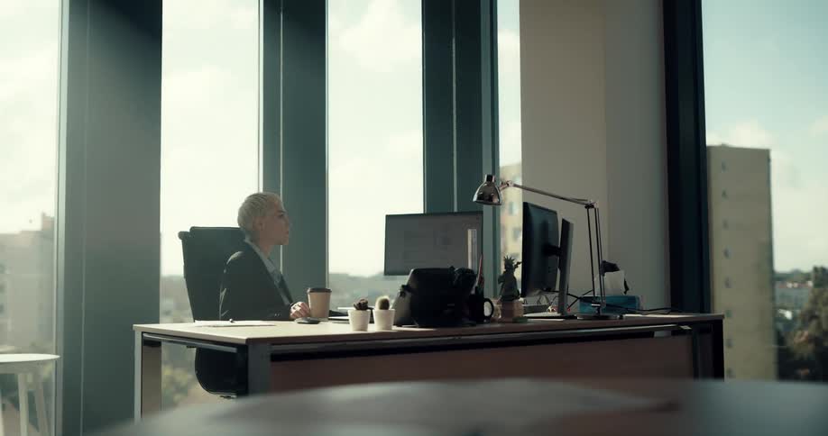 Businesswoman in suit sits at desk drinking coffee from cup using computer in the office