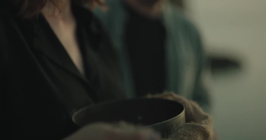 A young woman puts her hand in a bucket and picks up ashes and lets some run through her fingers and then throws them