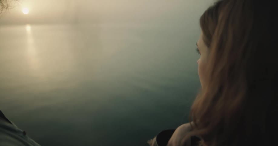 A woman picks up ashes from an urn to disperse them over the ocean at sunset