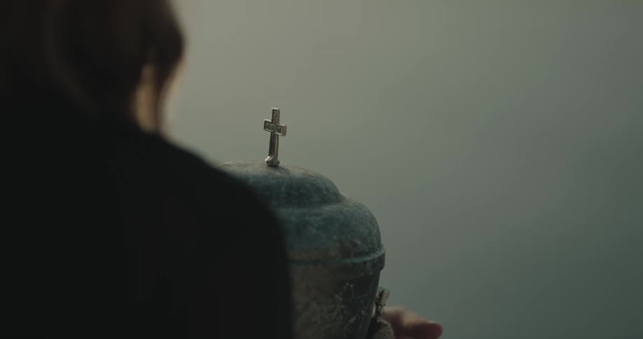 A person standing in front of the ocean opens an urn for ashes