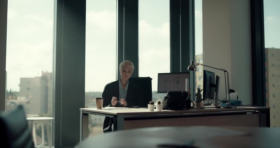 Woman sitting in office signs document before sitting back and drinking from to go cup