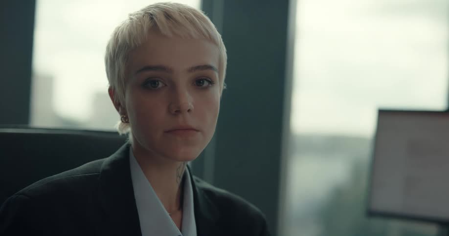 Businesswoman with short hair tattoo blazer jacket and shirt sits at desk looking at camera in the office