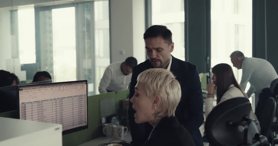 Blonde short haired woman sitting at a desk in the office talking to a coworker