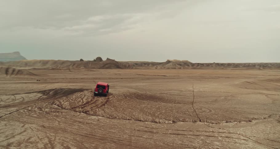 A red truck is traveling across the desert with mountains and mesa in the distance