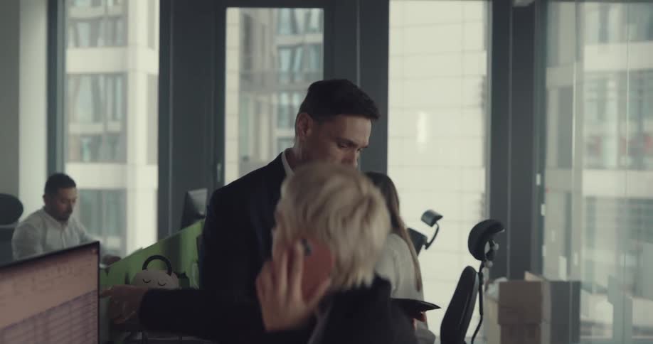Boss sitting over the desk of an employee in the middle of a busy office