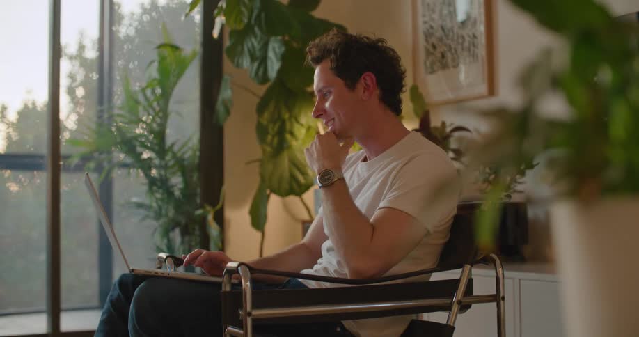 A man is sitting in a chair with a laptop computer having a video conversation with someone