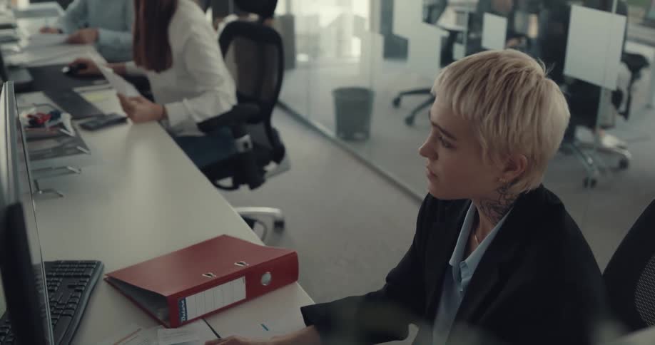 A man in an office yells at a woman as he points at his watch and then turns and yells at other employees before storming away