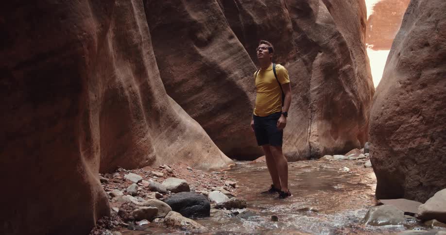 A man hiking through a ravine examines his surroundings before taking out his smartphone and raising it to take a photograph