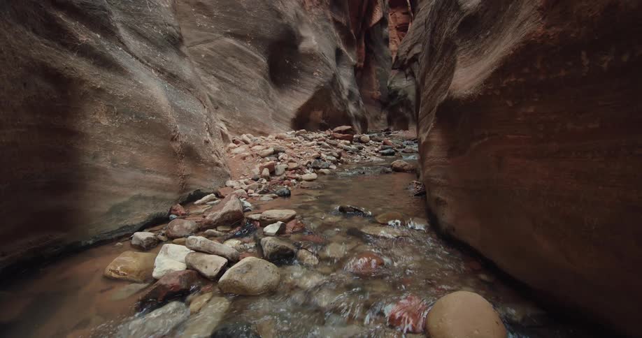 A shallow stream flowing over rocks between the walls of a narrow canyon