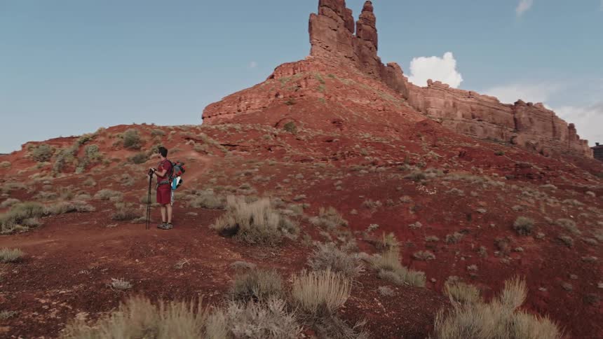 A hiker walking through the desert badlands stops to admire the mesa and rock formations