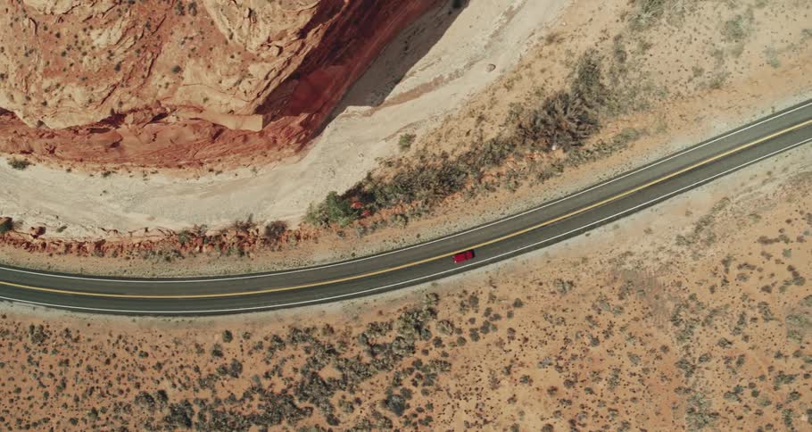 Aerial view of a red truck traveling on a road through the desert badlands with mountains and mesa on the roadsides