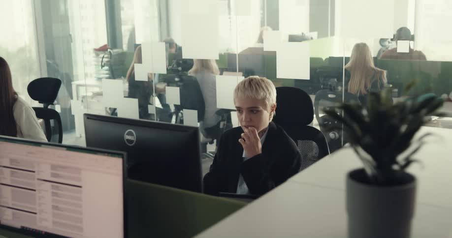 A woman sits at an office desk looking at a computer monitor