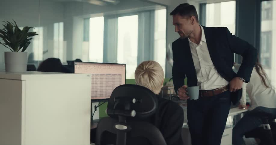 A female office employee talks with another man walking towards her desk