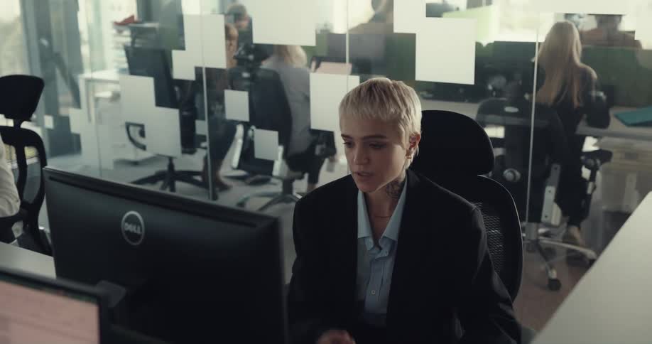 A woman looks around her monitor for help while sitting at her desk