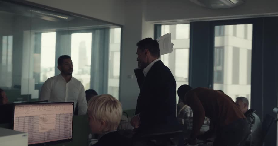 A man walks around an office full of people waving papers in the air and yelling