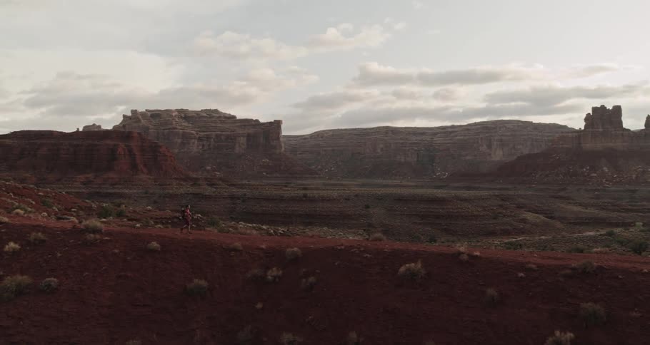 A man is hiking in a canyon with rock formations on a cloudy evening