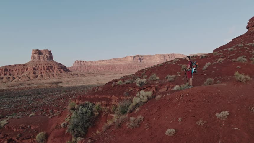 A hiker standing on a hill in the badlands looks out at the vast wilderness before him