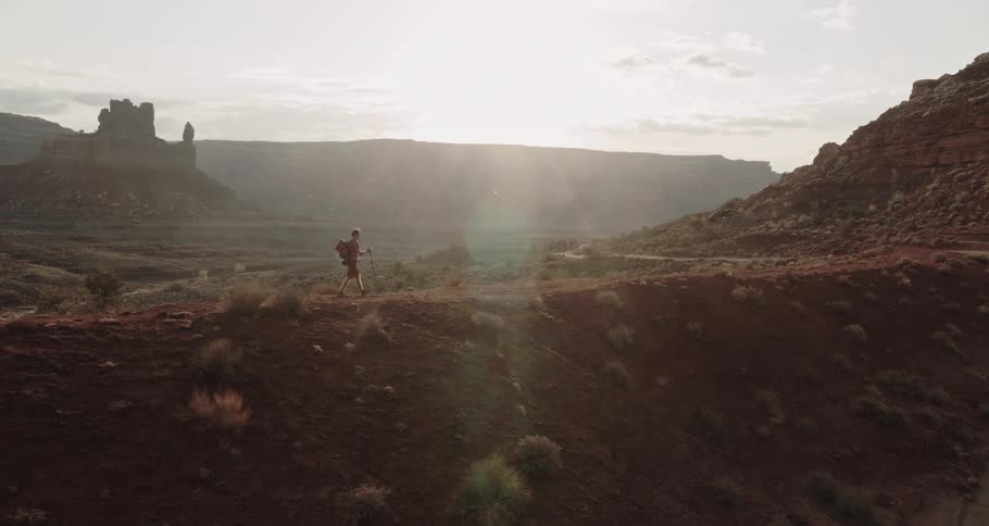 Man with a backpack hikes over a hill near the mountains in the badlands