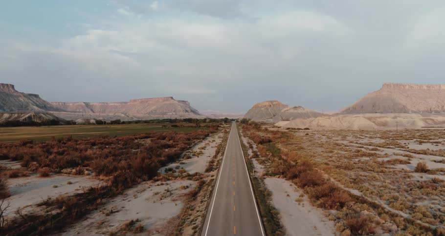 A highway road through the badlands with mountains and mesa under a cloudy sky