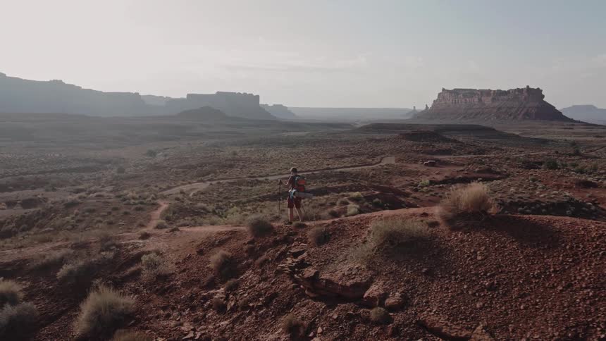 Man hikes along path through scrub land with mist covered mesa on the horizon
