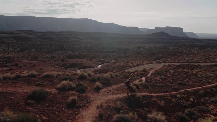A man using trekking poles hikes along a dirt trail through the badlands during the day