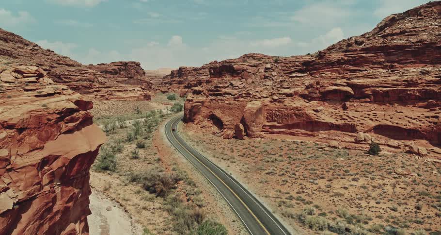 A red truck travels on highway road through desert canyons under a cloudy sky