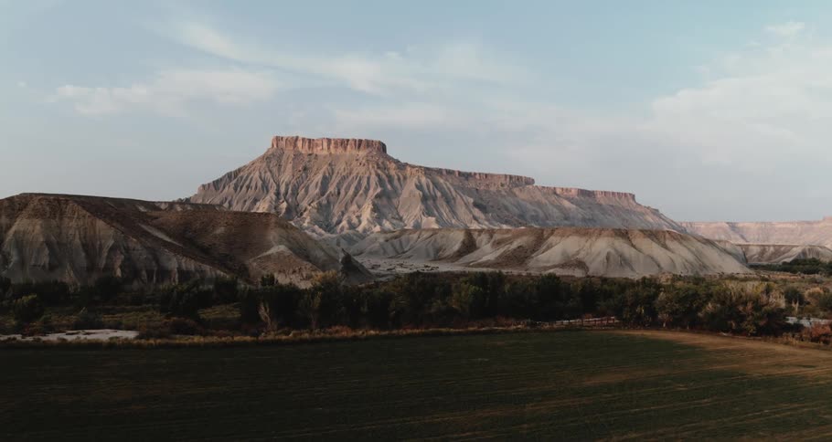 Mesas are high in the sky across the land and on the other side of trees under a cloudy sky