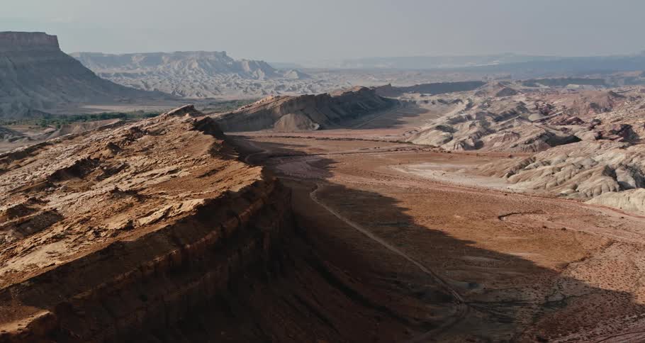 A mountain ridge and rough mountainous terrain in the desert with mesa in the distance under a hazy sky
