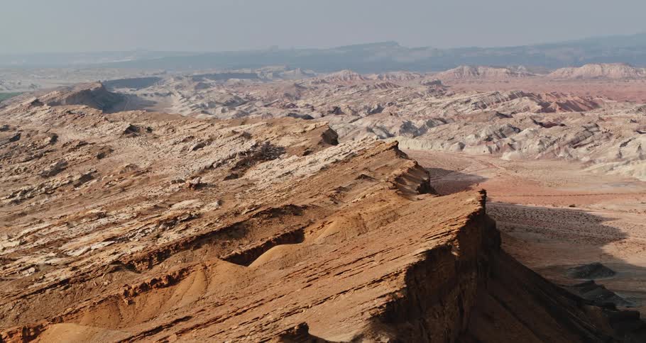 A mountain ridge and rough mountainous terrain in the desert with mesa in the distance under a hazy sky