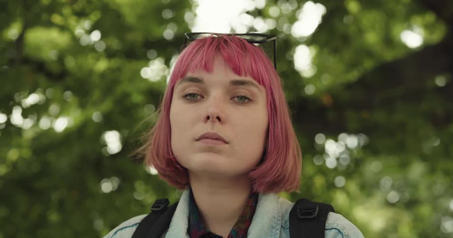 A woman with dyed pink hair turns her head to look straight ahead