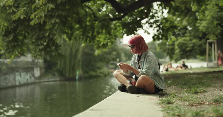 A woman sits near the canal and eats