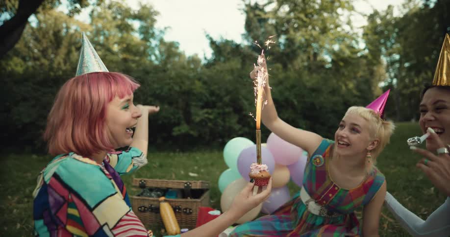 A woman brings a cupcake to a birthday party in the yard