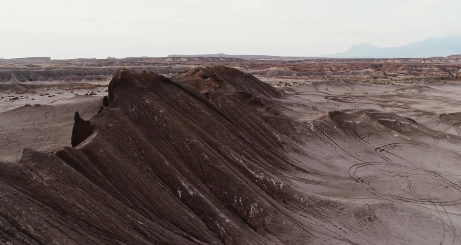 A mountain ridge and rock formations in the desert badlands and mountains in the distance under a hazy sky