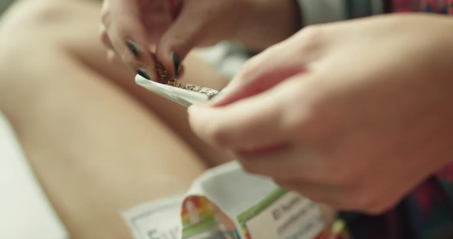 A woman is rolling a cigarette and sitting outdoors